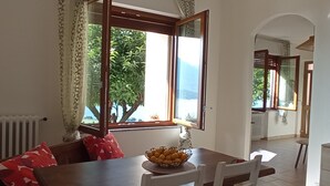 A dining area with a wooden table, white chairs, and a bowl of fruit. - Las tres tajanas Apartment (Gravedona Ed Uniti)