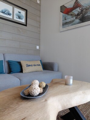 Un salon avec un canapé gris, une table basse sur laquelle se trouve un bol rempli d’objets décoratifs, et des œuvres d’art encadrées accrochées au mur.