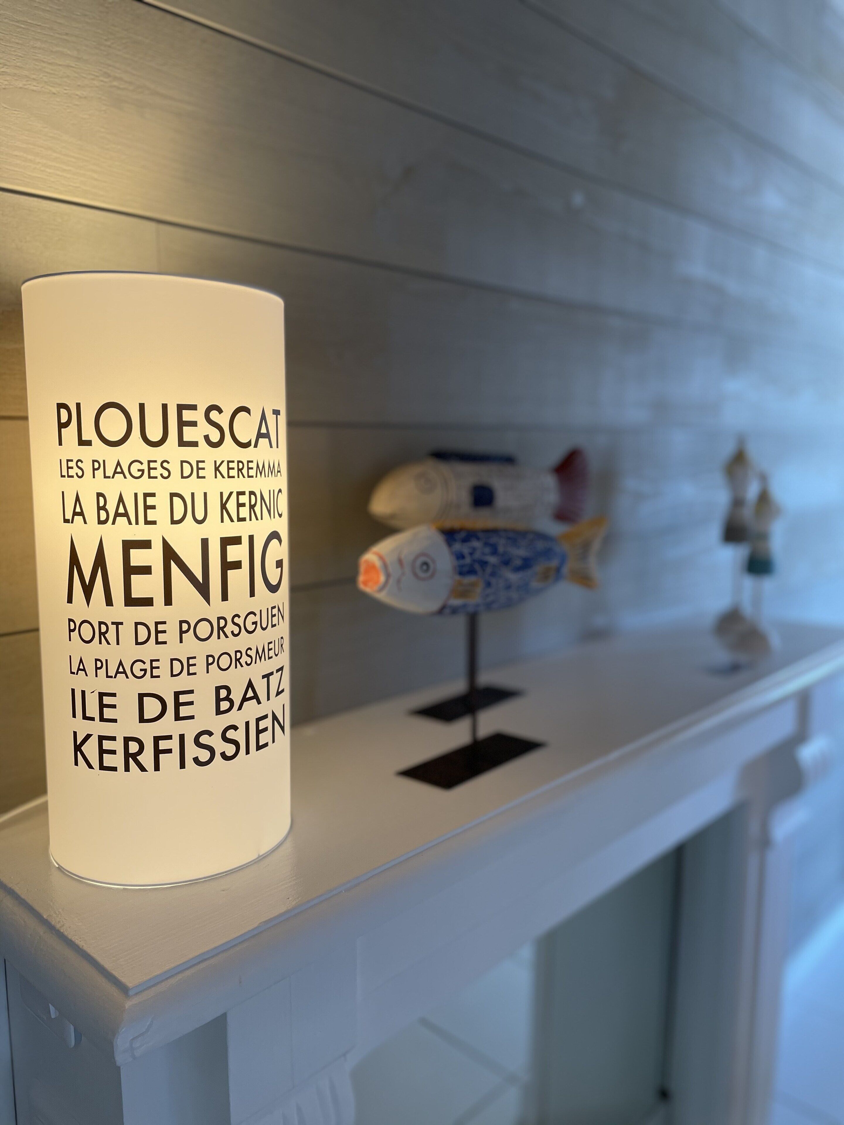 Um objeto cilíndrico branco com texto em francês, apoiado em uma lareira branca.