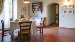 Un área de comedor con una mesa redonda, sillas, una estantería y un ventanal con cortinas.