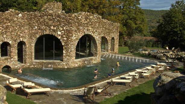 A stone building with arched windows and a pool area with lounge chairs.