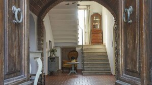 A hallway with a brick floor, a wooden chair, a small table, and a staircase leading to a door with a mirror.
