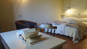 Une chambre à coucher avec un lit, une chaise, une table avec des livres et une lampe de chevet.