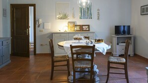 Un coin repas comprenant une table ronde, quatre chaises, un lustre et un téléviseur posé sur un meuble.