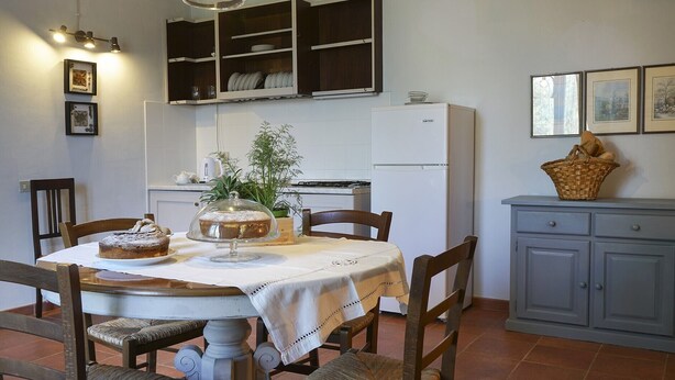 Un espace repas comprenant une table ronde, des chaises, un buffet, un réfrigérateur et un meuble surmonté d’un panier.