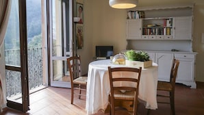 Un coin repas comprenant une table, des chaises, une nappe blanche, un luminaire suspendu, une bibliothèque et une vue à travers une porte vitrée.