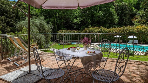Een terras met een tafel, stoelen, een zwembad en een omheining.