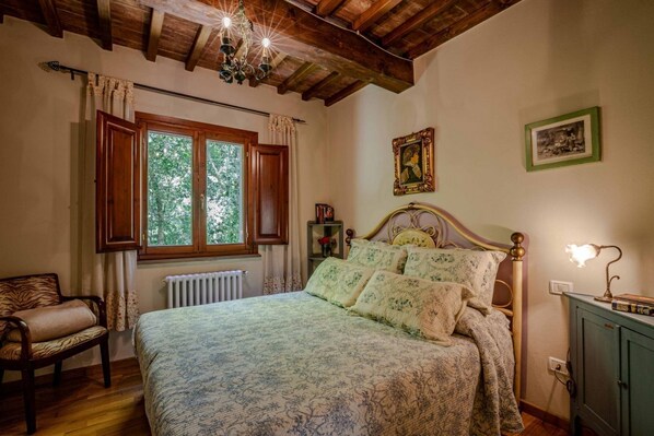 Une chambre avec un plafond en bois, un lit avec une literie à motifs, une chaise et un radiateur.