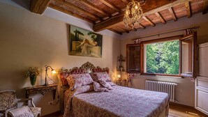 Ein Schlafzimmer mit einem großen Bett, Holzbalkendecke, einem Fenster mit Blick auf Bäume und einem Gemälde an der Wand.