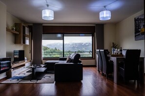 Un salon moderne doté d’une grande fenêtre, d’un canapé, d’une table basse et d’un coin repas avec des chaises.