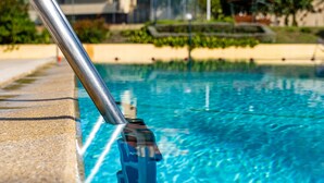 En swimmingpool med klart blåt vand, en metalstige og udsigt til bygninger og træer i baggrunden.