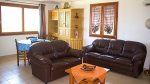 Un salon comprenant deux canapés en cuir marron, une table basse en bois, une table à manger avec des chaises et un meuble contenant des objets décoratifs.