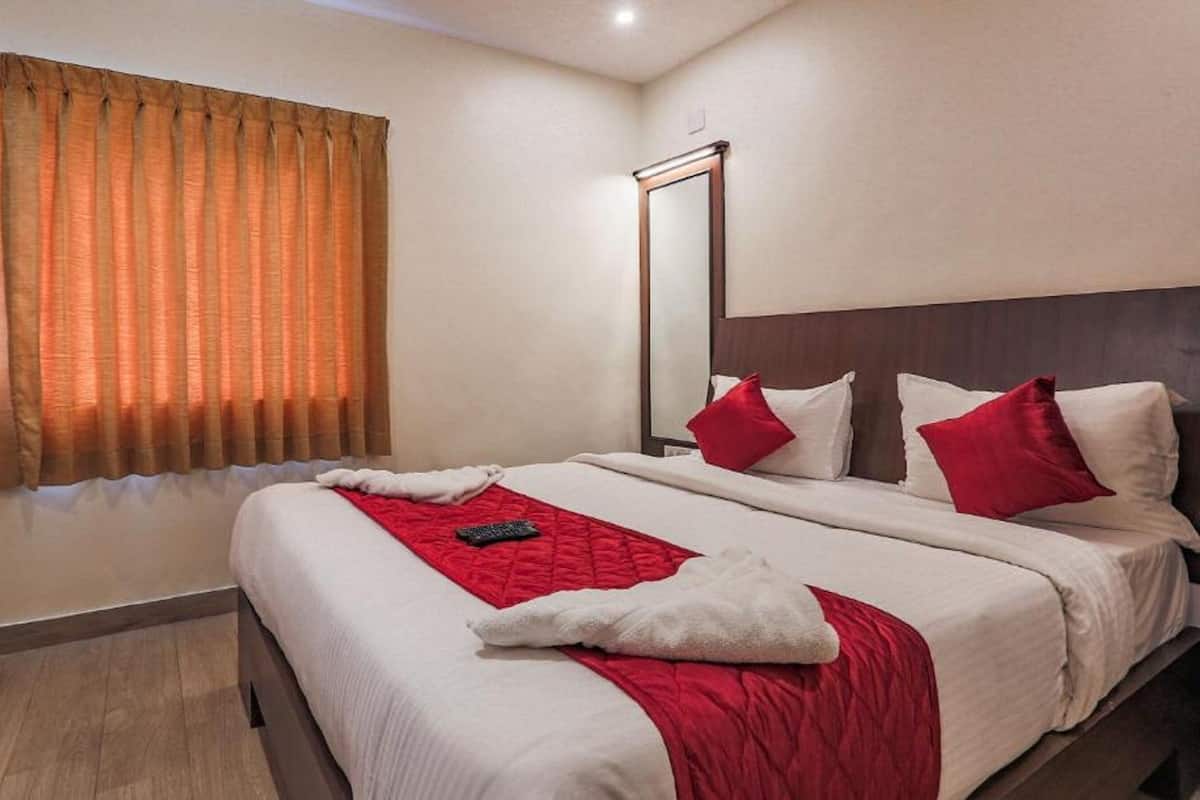 A hotel room with a large bed, red and white bedding, a mirror, and a window with orange curtains.