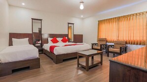 Habitació d'hotel amb dos llits individuals, un sofà, una taula petita i una finestra gran amb cortines.