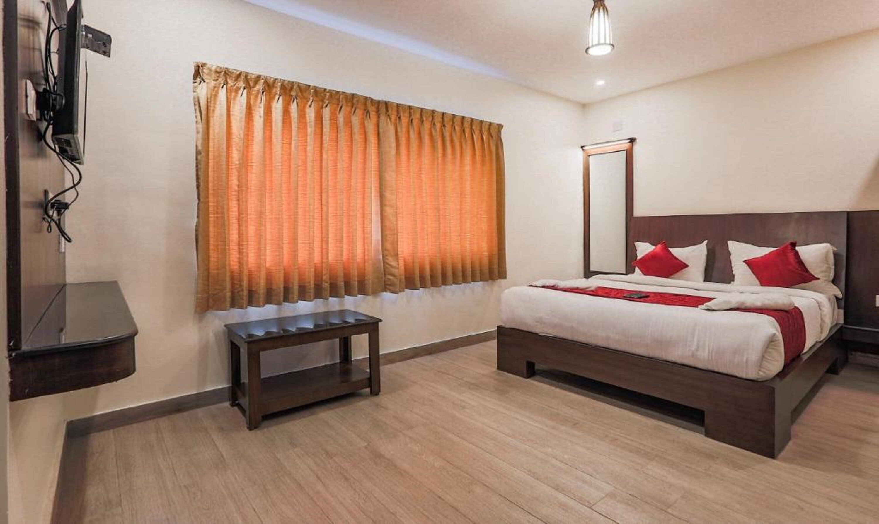 Una camera d'albergo con un letto, un comodino, uno specchio e una finestra con tende.