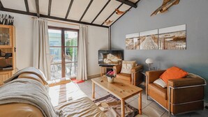 Una sala de estar acogedora con un sofá, una mesa de centro y un televisor. Hay una ventana con cortinas, un mueble de madera y una pared decorada con obras de arte.