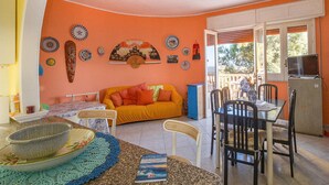 En hyggelig stue med en lys orange væg, en gul sofa, et spisebord med stole og et køleskab.