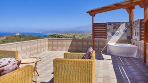 Eine Dachterrasse mit Korbmöbeln, einem Whirlpool und Blick auf das Meer und die Hügel.