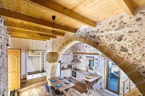 A rustic kitchen with stone walls, wooden beams, and a dining area with a table set for four. - Achilleas Apartments  (Platanias)