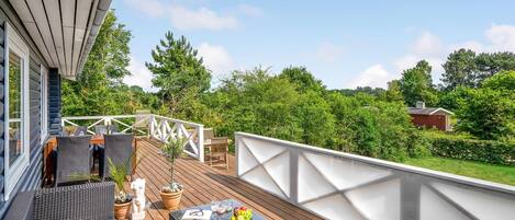 A wooden deck with outdoor furniture, a white railing, and a view of a forested area.