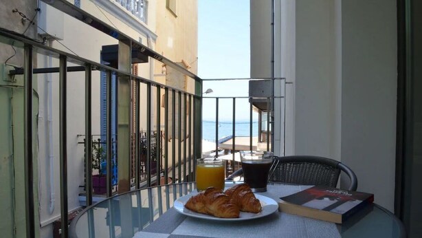 Ein Balkon mit Glastisch, einer Platte mit Croissants, einem Glas Orangensaft und einem Buch.