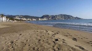 Ein sandiger Strand mit Fußspuren, ein klarer Himmel und Gebäude im Hintergrund.