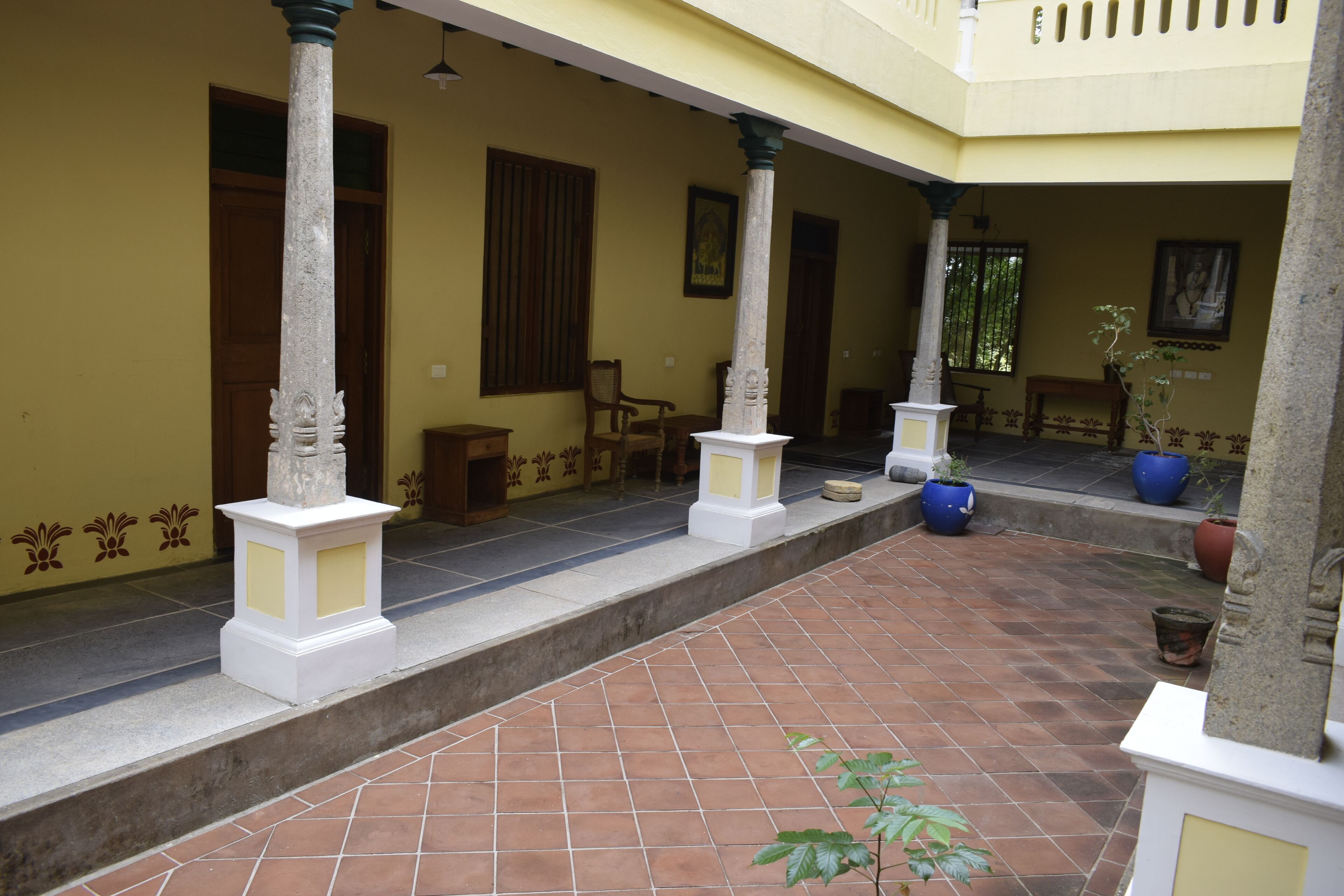 Un patio con suelo de baldosas, pilares blancos y plantas en macetas.