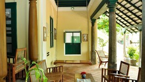 A covered outdoor seating area with wooden furniture and a swing. - Saradharam Heritage Hotel Lakshmi Vilas (Kattumannarkoil)