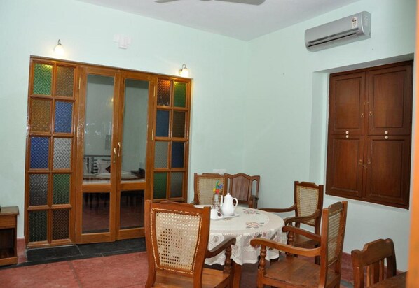 Un comedor con una mesa redonda, cuatro sillas de madera, un mantel blanco y un aparador de madera.