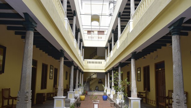 A covered corridor with columns, potted plants, and a staircase leading to an upper level. - Saradharam Heritage Hotel Lakshmi Vilas (Kattumannarkoil)