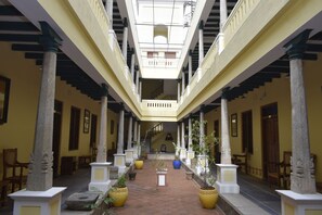 Un pasillo cubierto con columnas, plantas en macetas y una escalera que lleva a un nivel superior.