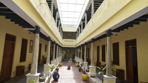 A corridor with a high ceiling, columns, and potted plants. - Saradharam Heritage Hotel Lakshmi Vilas (Kattumannarkoil)