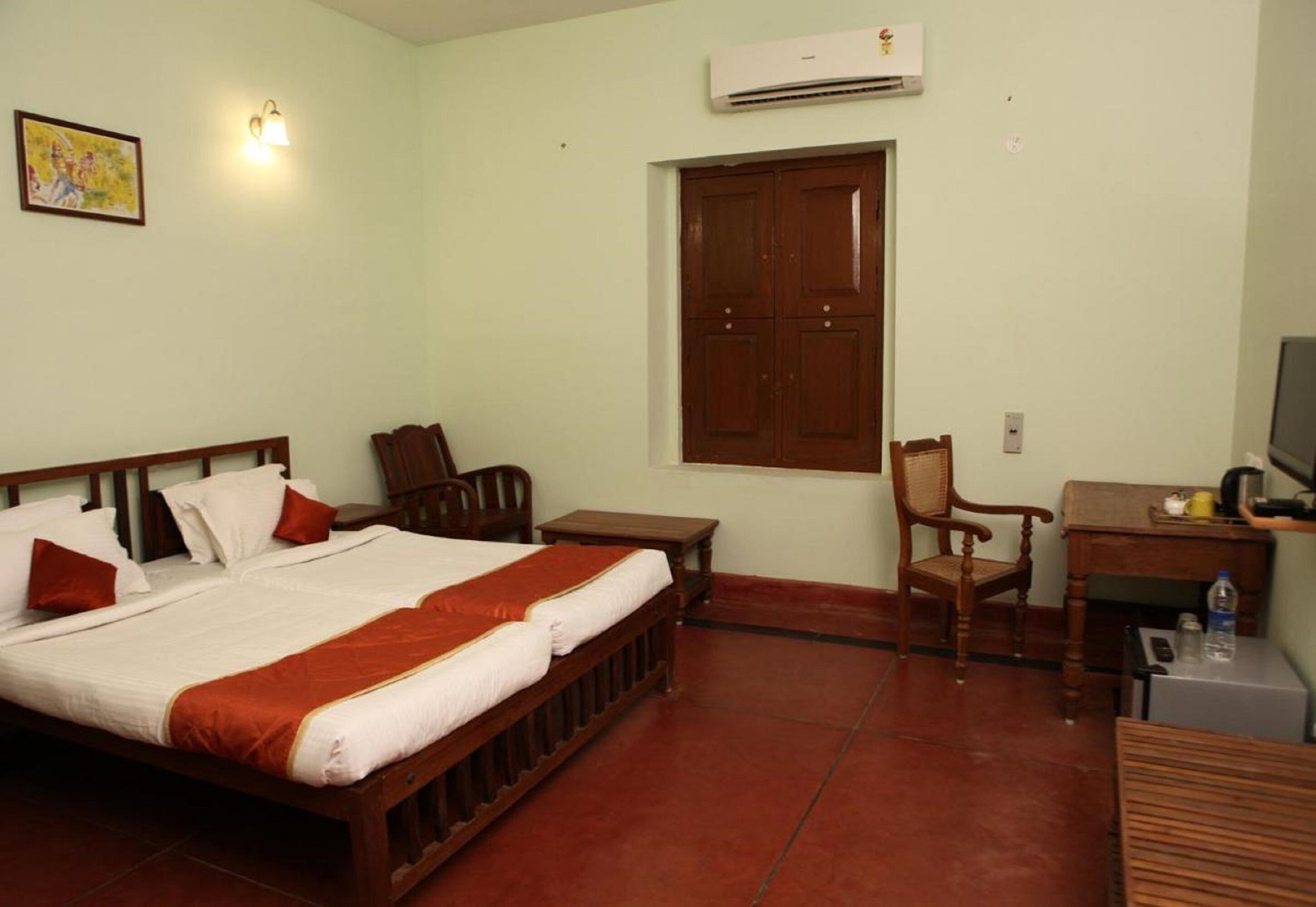A hotel room with a bed, a desk, a chair, an air conditioner, and a window.