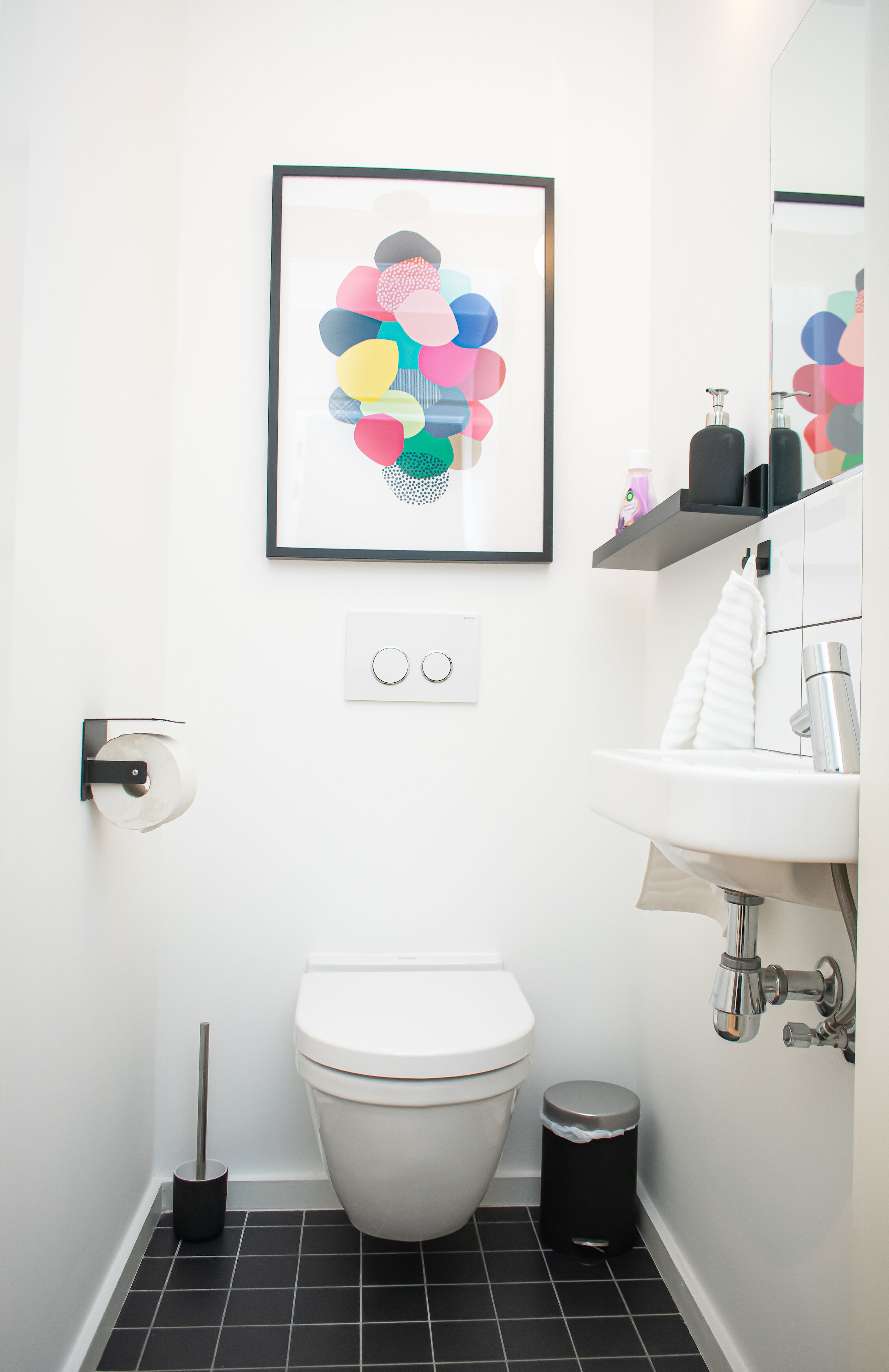 Une salle de bain moderne avec des toilettes, un lavabo et une œuvre d’art encadrée accrochée au mur.
