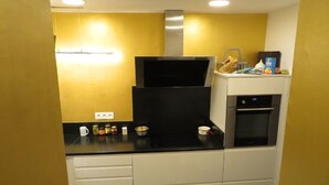 A kitchen with a black countertop, white cabinets, a stainless steel range hood, and a microwave.