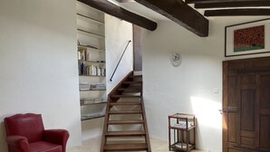 A staircase leading to a loft area with a red leather chair, a small wooden table, and a bookshelf filled with books.