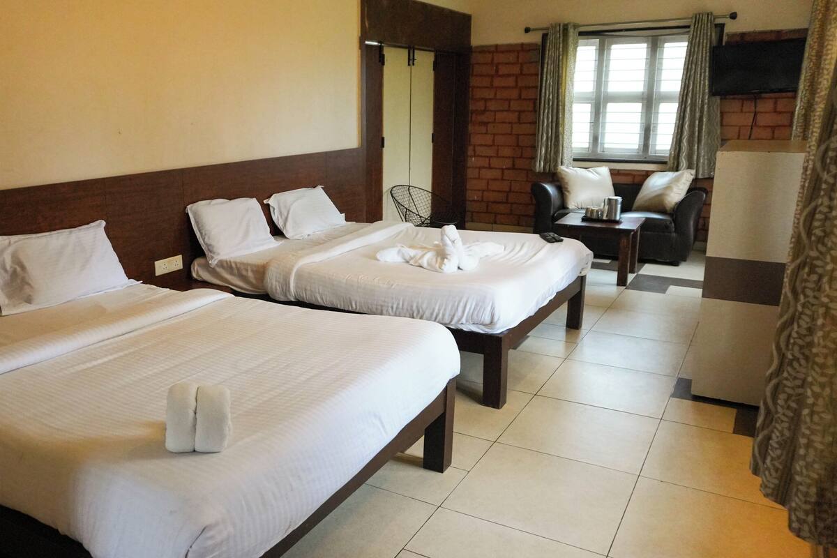 A hotel room with two beds, a small table, a chair, and a TV.