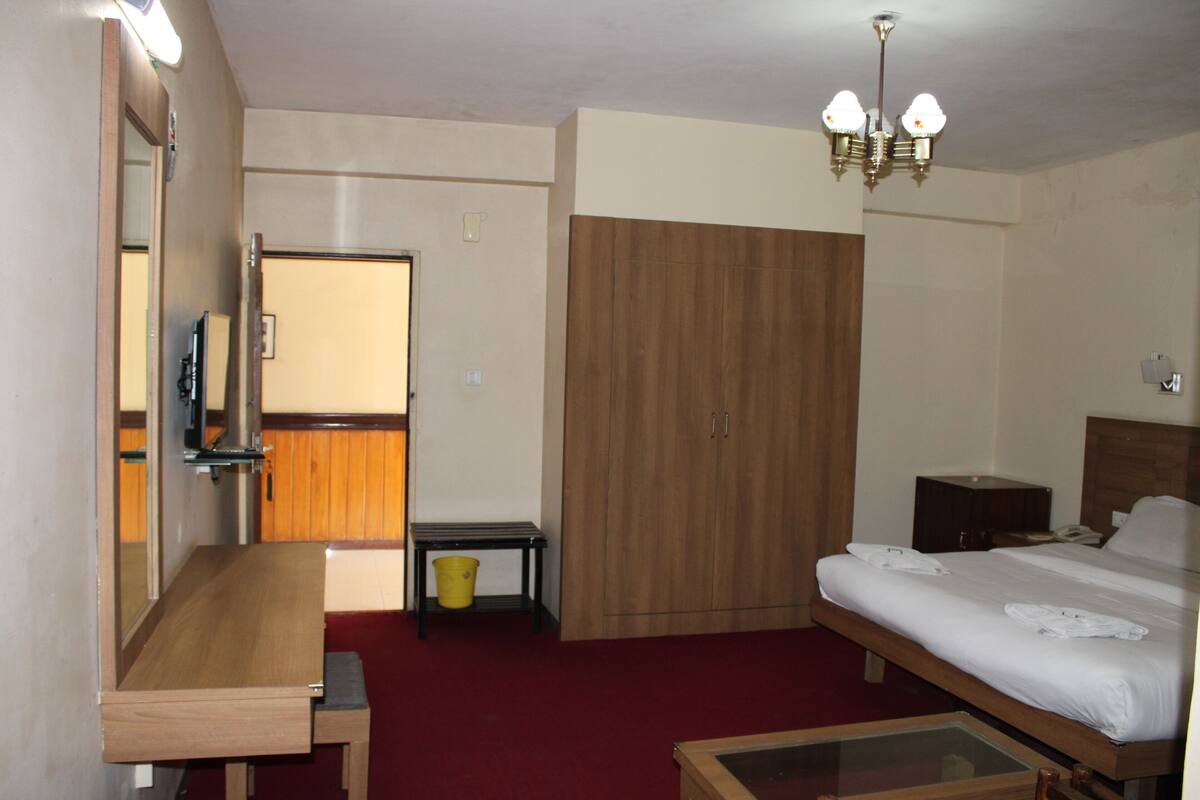 A hotel room with a wooden bed, a desk with a mirror, a small table, a wardrobe, and a chandelier.