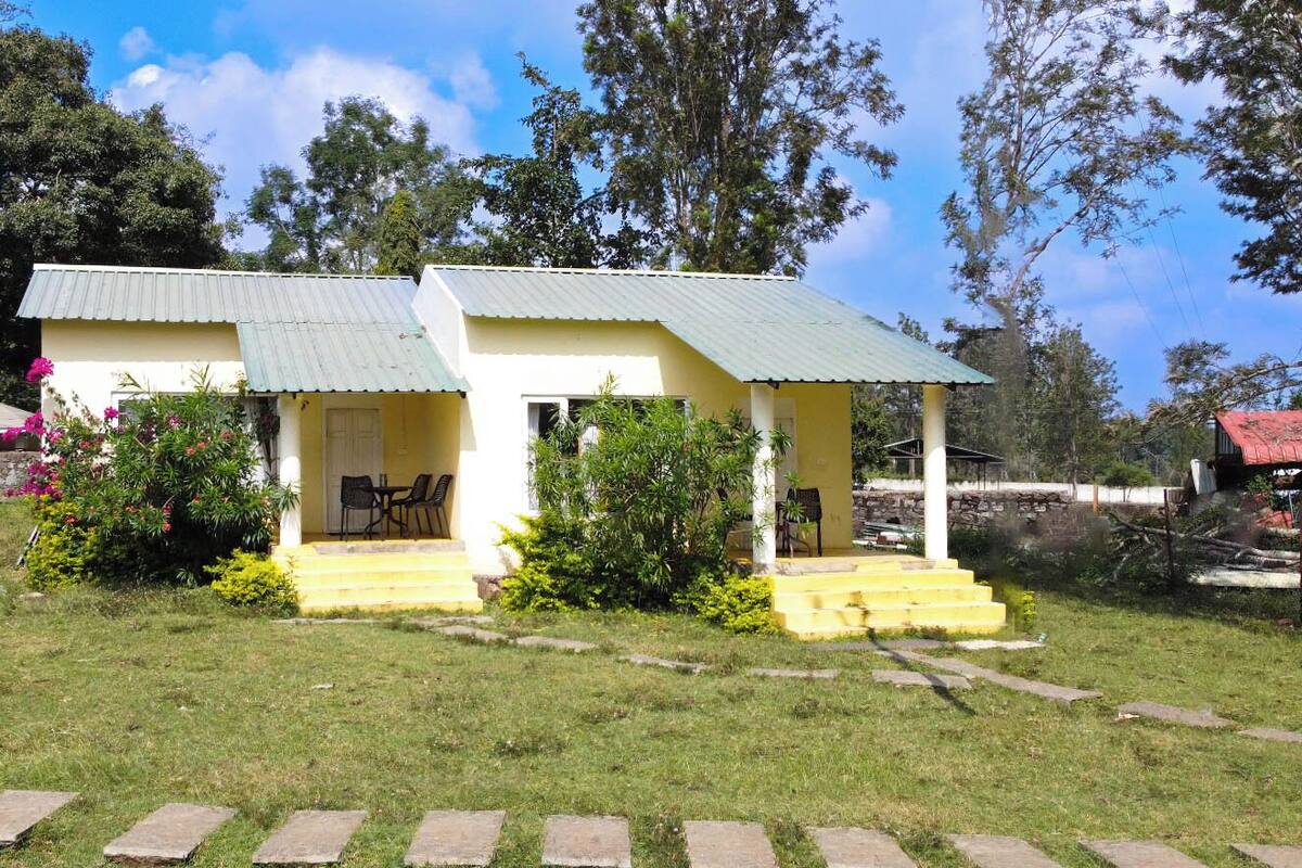 A small, single-story building with a green roof and yellow walls, featuring a porch with outdoor seating.