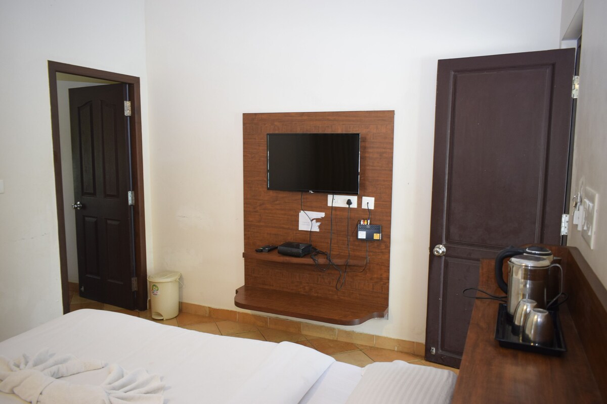 Ein Hotelzimmer mit einem Bett, einem an einer Holzplatte montierten Fernseher, einer Kaffeemaschine auf einem Holztisch und einem Mülleimer.