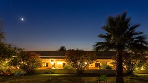 A well-lit building with a patio area, including chairs and a hammock, under a night sky with visible stars. - Maisons de L'algarve Location C 3 (Estoi)