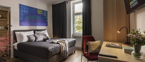 A modern bedroom with a bed, a desk, a chair, a TV, and a window with curtains.