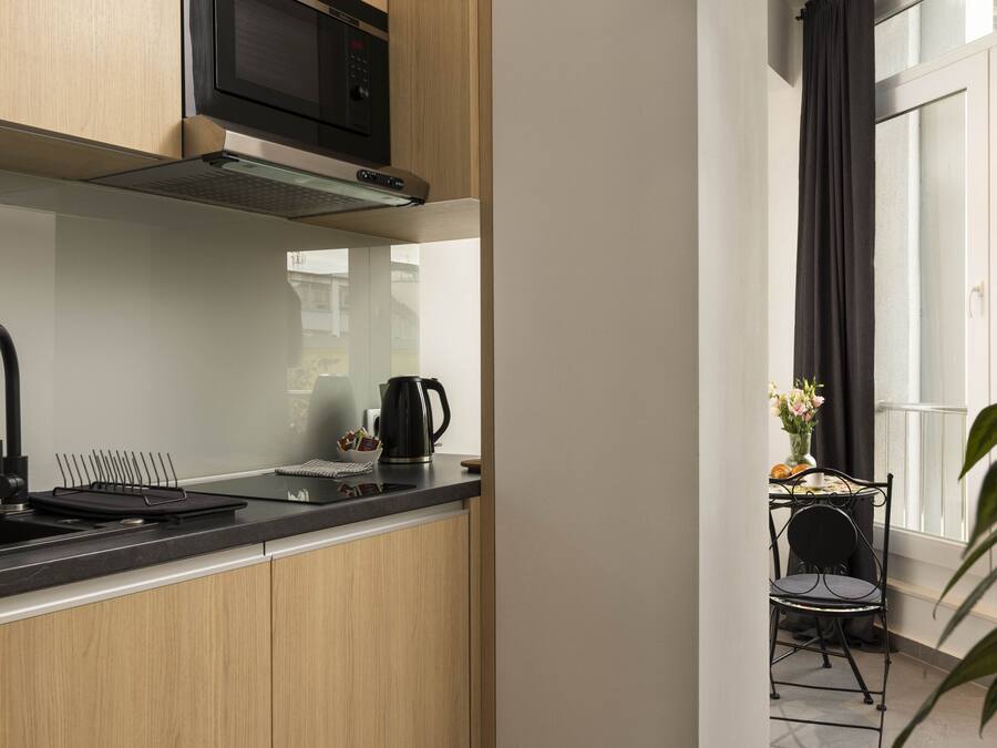 A modern kitchen with a microwave, sink, and kettle. There is a window with curtains and a view of the outside.
