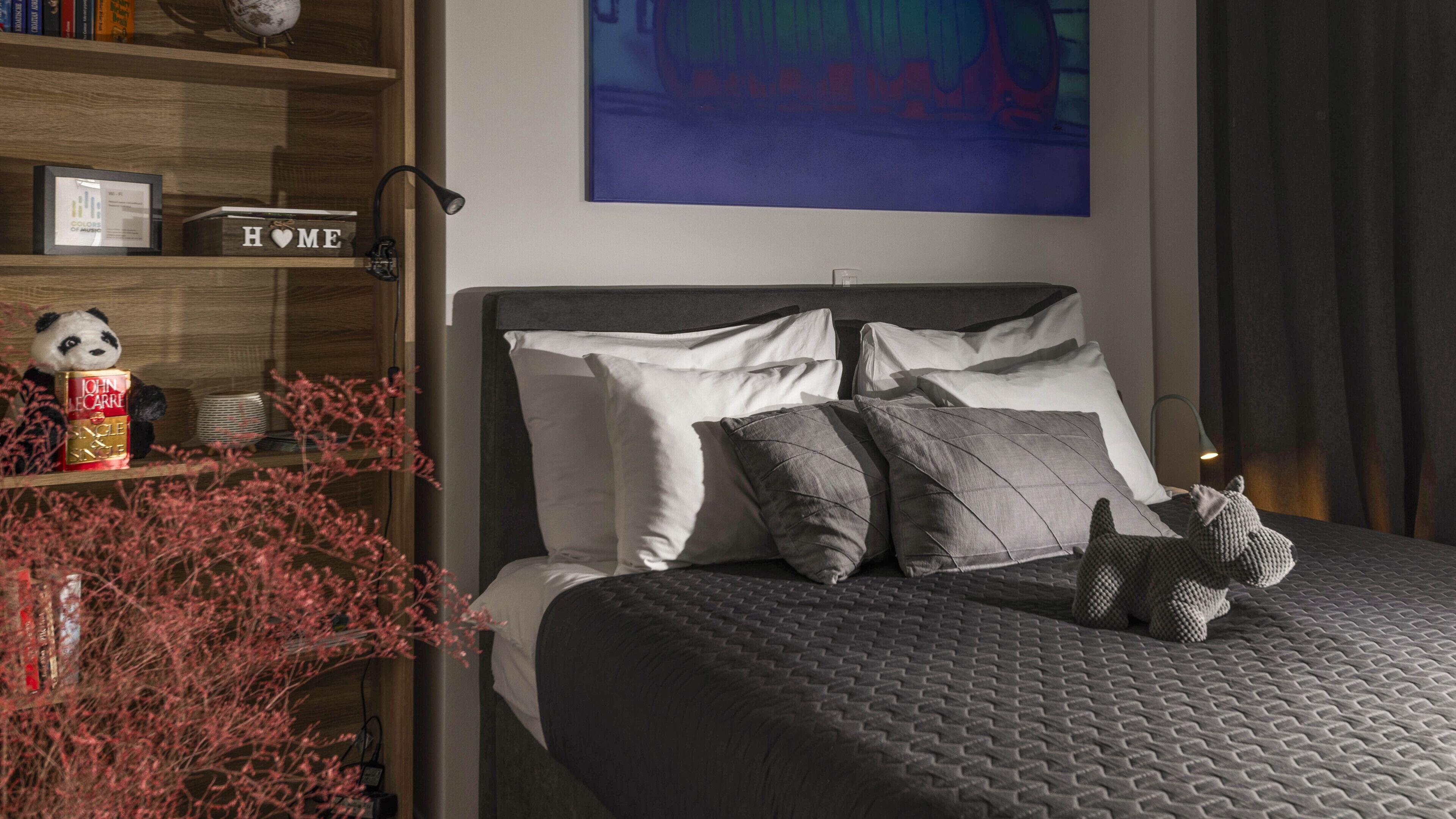 Un dormitorio moderno con una cama, almohadas, una estantería y un cuadro en la pared.