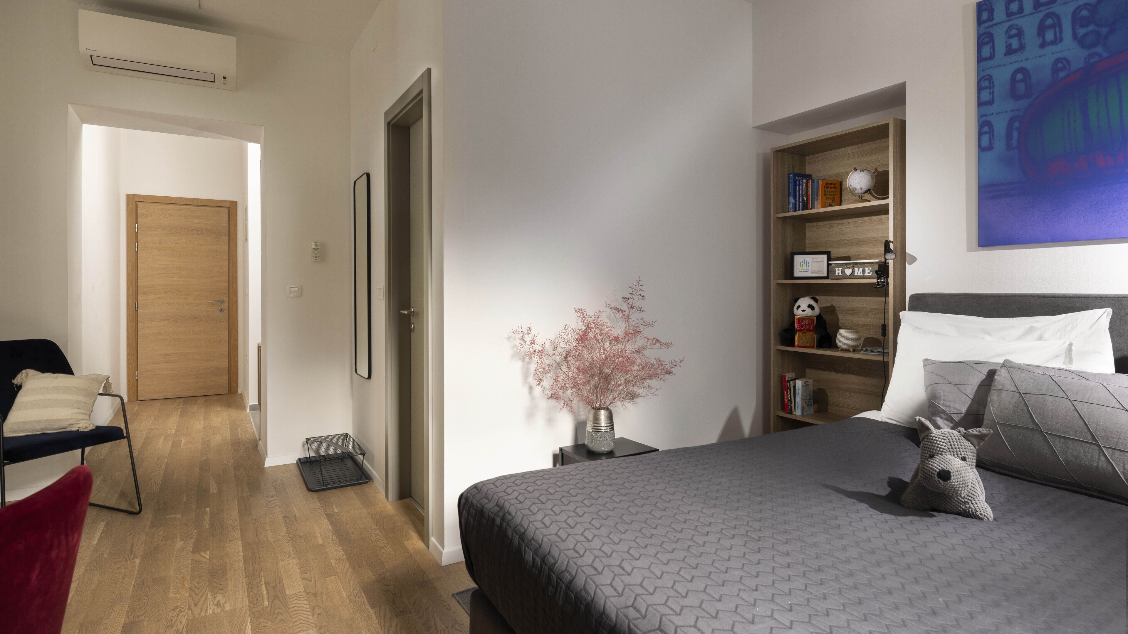 A bedroom with a bed, bedside table, lamp, and a bookshelf.