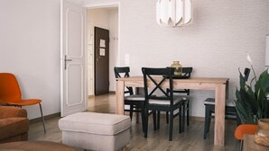 Zona pranzo con tavolo e sedie in legno, lampadario a sospensione e porta che dà su un'altra stanza.