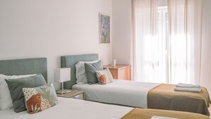 Una camera d'albergo con due letti, un comodino con lampada, un quadro appeso e una finestra con tende.