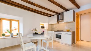 A modern kitchen with white cabinetry, a round dining table with white chairs, and wooden beams on the ceiling. - DeAmicis Studios by Irundo (Rovinj)