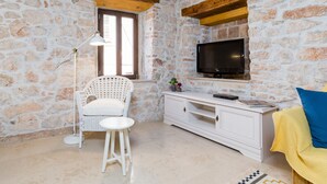 A room with stone walls, a white wicker chair, a small white table, a white TV stand, and a yellow sofa. - DeAmicis Studios by Irundo (Rovinj)