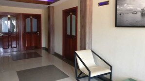 A hallway with wooden doors, a framed picture on the wall, and a chair in the foreground. - French Avenue (Mahe)